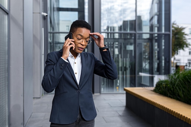 Serious and nervous business woman with glasses African American woman with short haircut talking on the phone outside the office