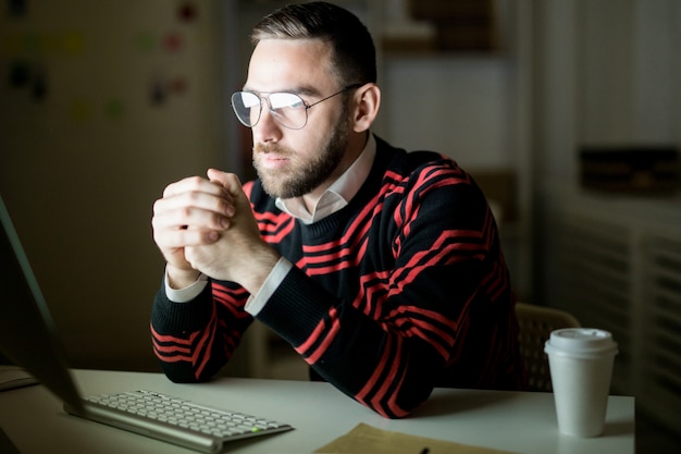 Serious office employee working with computer in dark office