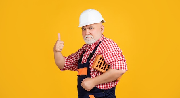 Serious old aged man bricklayer in helmet on yellow background