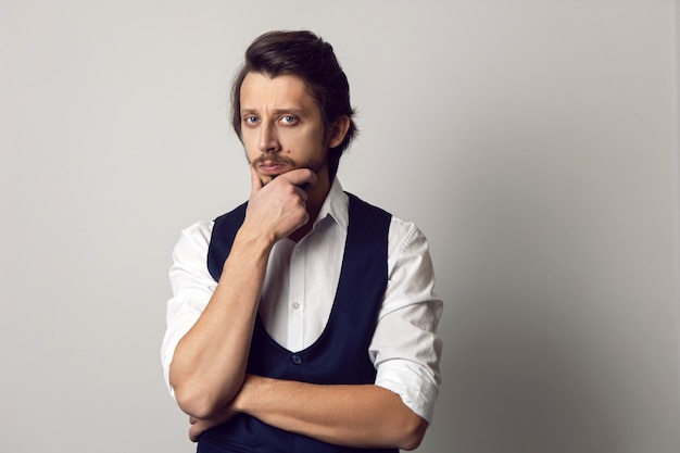 Serious portrait of a man in a vest in a white shirt on a white wall