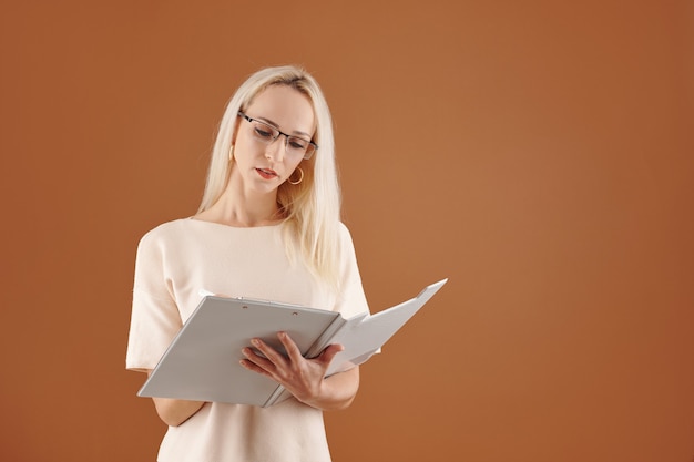 Serious pretty female teacher reading document in clipboard and taking notes