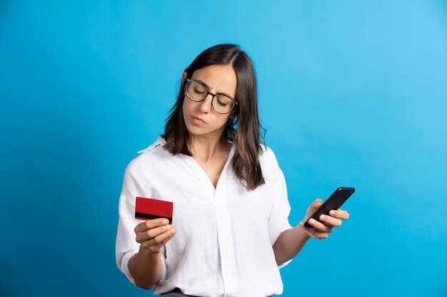 Serious pretty hispanic woman holding phone and credit card