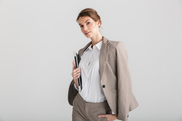 serious pretty woman in formal suit posing with laptop on camera isolated over white background