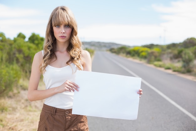 Serious pretty woman holding sign while hitchhiking 