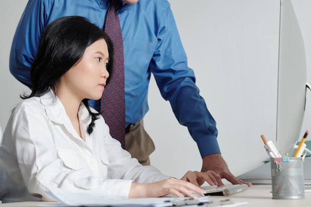 Serious pretty young businesswoman working on computer under control of her boss