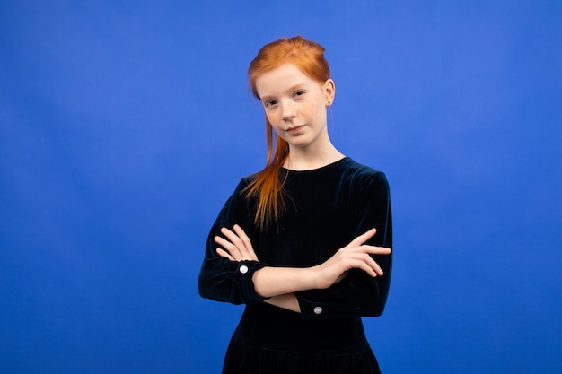 Serious red-haired teenager girl with arms crossed on a blue