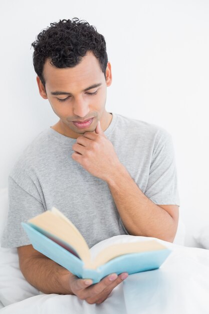 Serious relaxed man reading book in bed