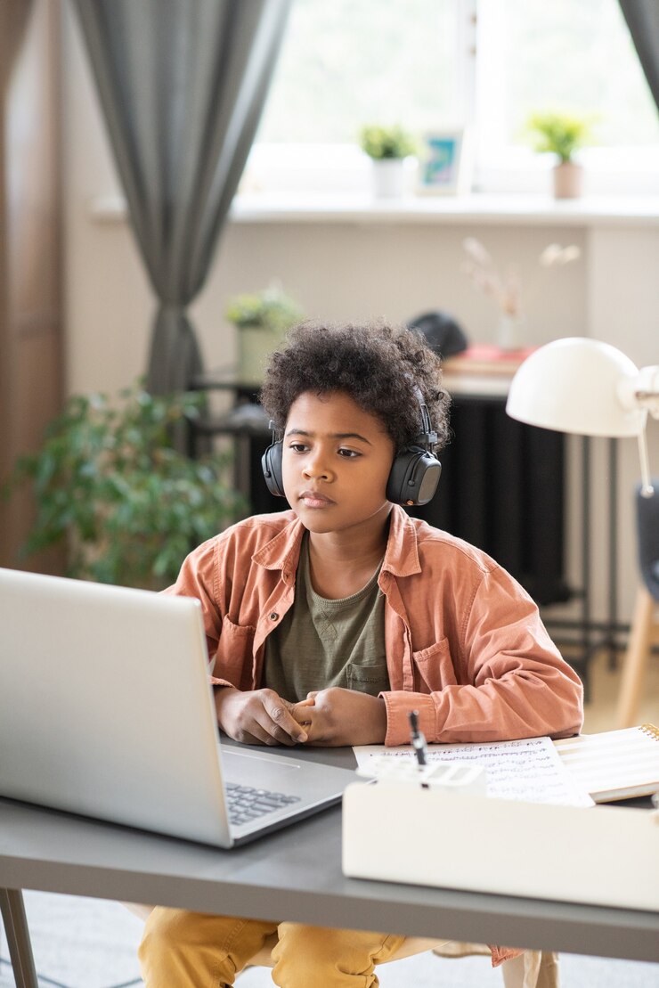 Photo serious schoolboy in headphones sitting in front of laptop