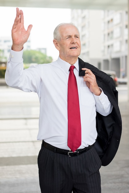 Serio uomo d'affari senior tenendo la giacca sopra la spalla e alzando la mano