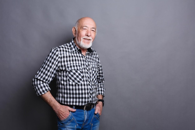 Serious senior man posing with hands on hips, gray studio background, copy space