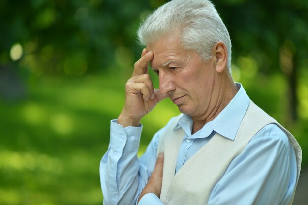 Serious senior man thinking in park on green background