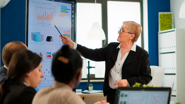 Serious senior manager executive and diverse team people analyzing digital project presentation briefing, sharing ideas in teamwork, discussing financial plan in office corporate meeting room