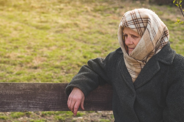 Serious senior woman sitting on bench and looking away. Portrait of thoughtful old grandmother leaning on cane