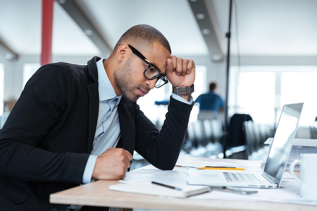 Serious smart businessman thinking about something using laptop in the office