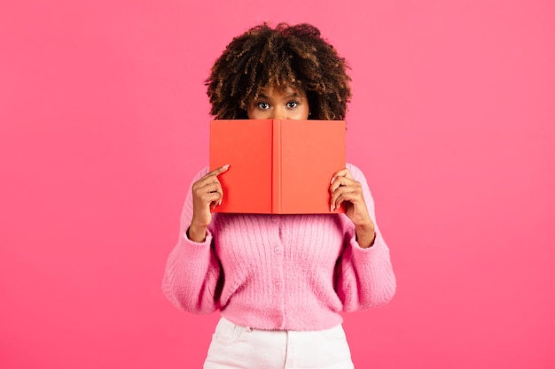 Serious smart millennial african american curly female student in casual hiding behind book or diary