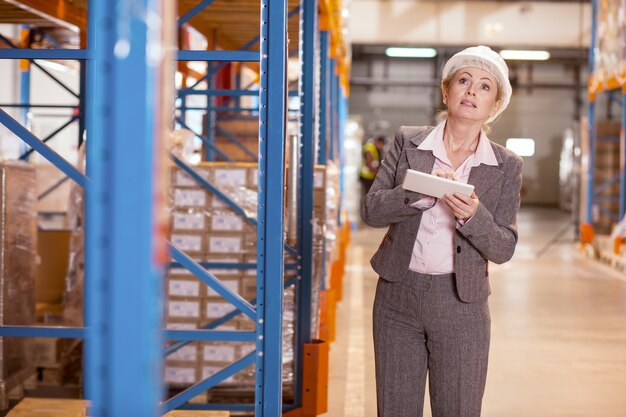 Donna intelligente seria che osserva in su mentre controlla il processo di lavoro nel magazzino