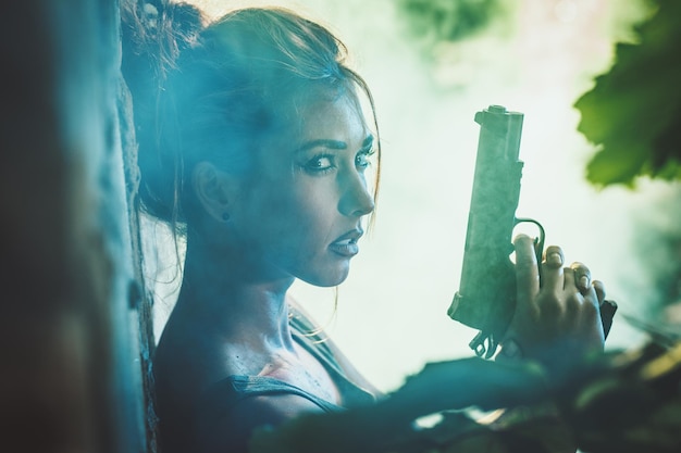 Photo serious soldier woman holding gun and getting ready for the attack in abandoned ruin.