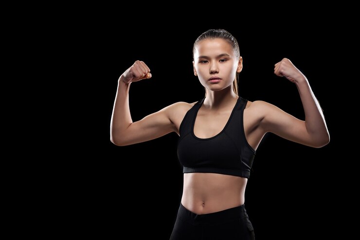 Photo serious sporty girl in black activewear standing in isolation while showing her physical strength
