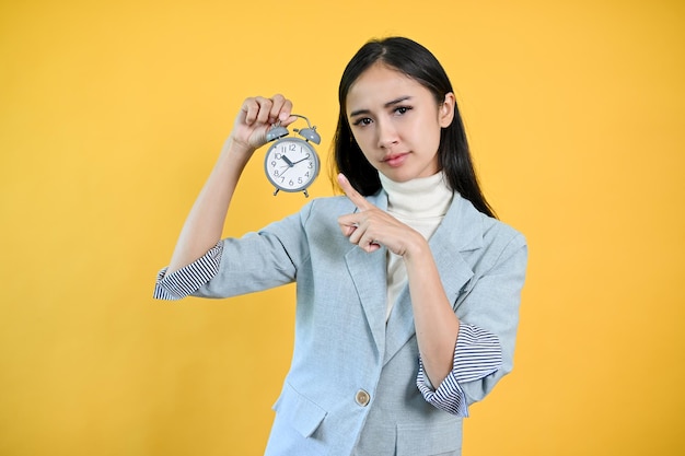 A serious and strict Asian businesswoman pointing her finger at an alarm clock