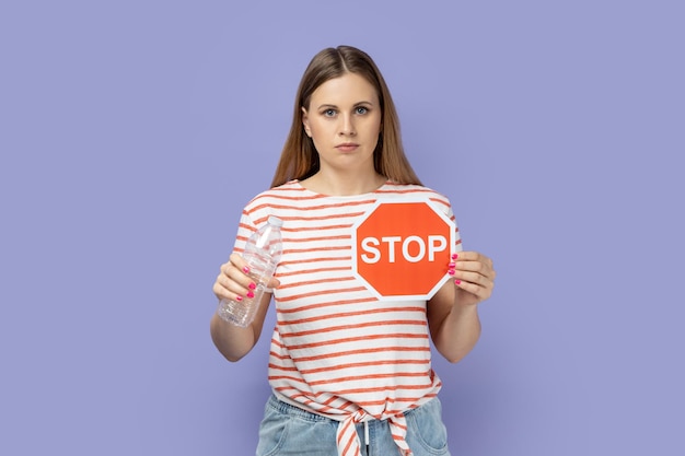 Serious strict bossy woman showing red stop sign and holing plastic bottle in hands