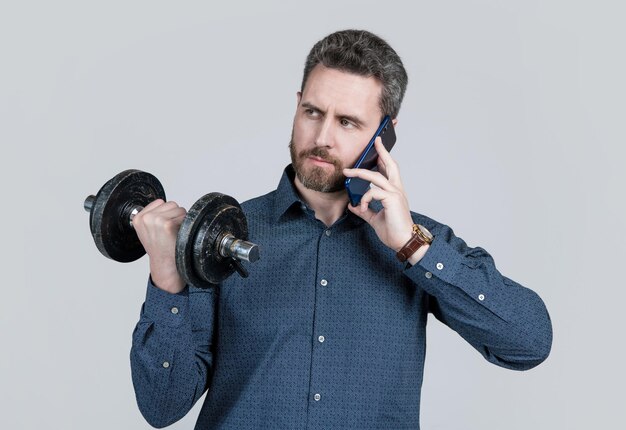 Серьезный сильный бородатый мужчина бизнесмен тренируется со штангой и разговаривает по телефону, бизнес.