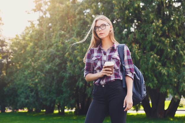 공원에서 커피 컵을 들고 서 있는 진지한 여학생은 대학 캠퍼스에서 휴식을 취하고 공간을 복사합니다. 커뮤니케이션, 교육 개념