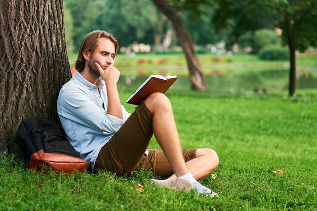 Lo studente serio nel parco della città universitaria ha letto un libro