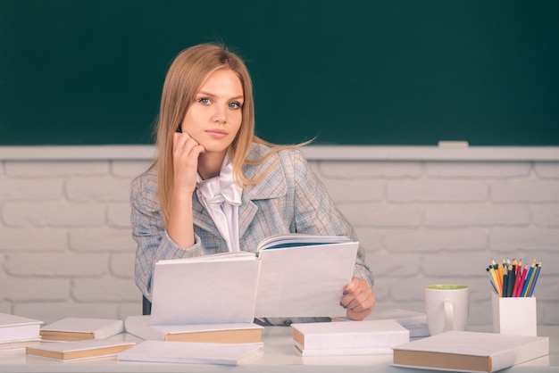 Serious student reading book on blackboard background with copy space portrait of young female colle...