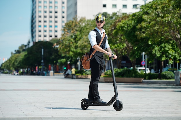 Serious stylish man in sunglasses and helmet riding on scooter