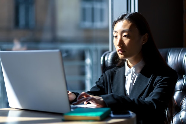 Serious and successful Asian business woman working in the office on a laptop, focused and thoughtful