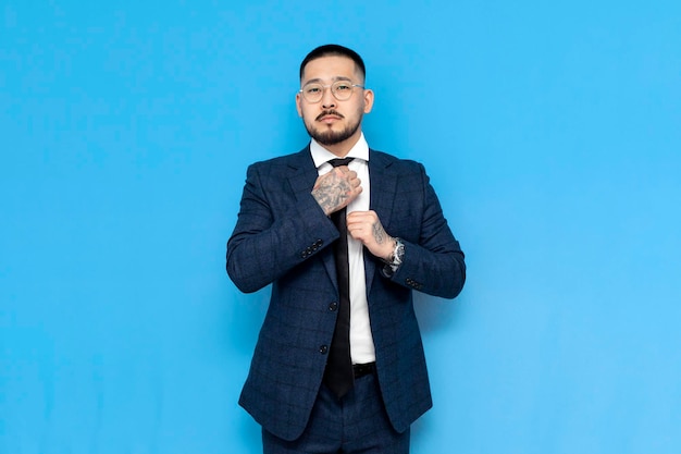 serious successful asian businessman in suit and glasses on blue isolated background