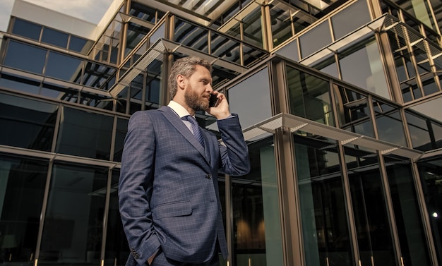 Серьезный успешный бородатый бизнесмен в официальном костюме говорит по телефону на смартфоне