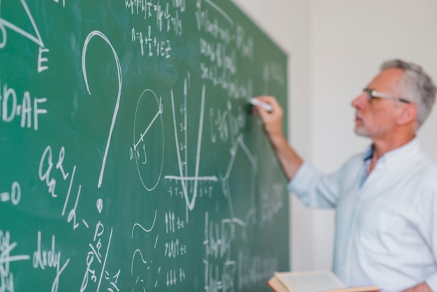 Serious teacher chalking on blackboard in soft focus