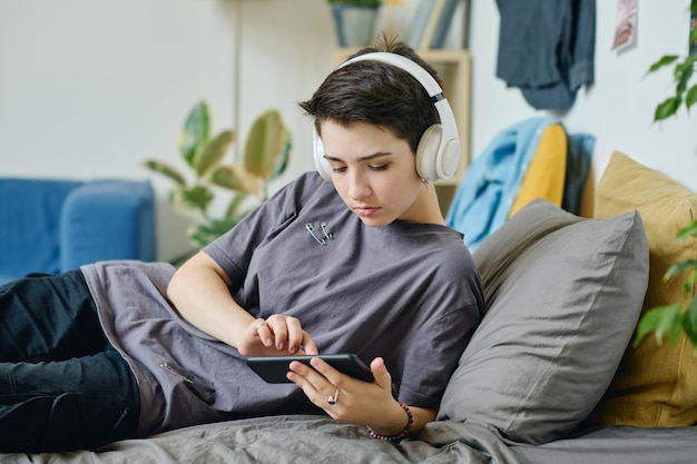 Serious teenage girl in grey tshirt and white headphones using smartphone