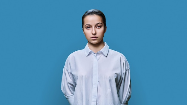 Serious teenage girl looking at camera on blue color background
