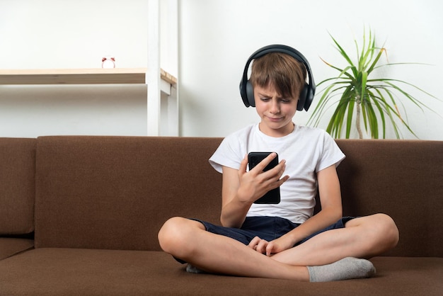 ワイヤレス ヘッドフォンで深刻な 10 代の若者が携帯電話の画面を見る 少年は音楽を聴いたり、映画を見たり