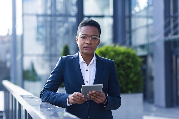 Donna d'affari seria e pensante afroamericana in pausa vicino all'ufficio, utilizza un tablet online, legge le statistiche utilizza l'applicazione