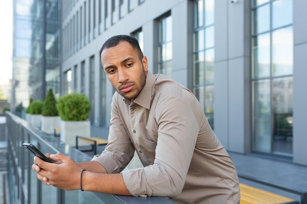 Serious thinking businessman outside office building pondering decision african american worker sad