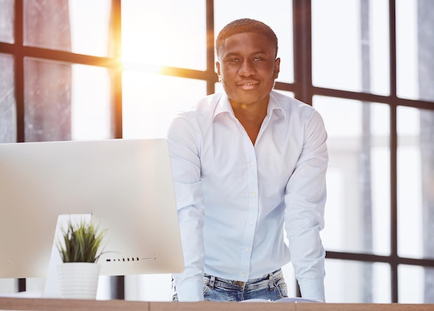 Serious thoughtful millennial businessman standing leaning on desk in home office loft interior