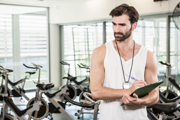 Serious trainer writing on clipboard at the gym