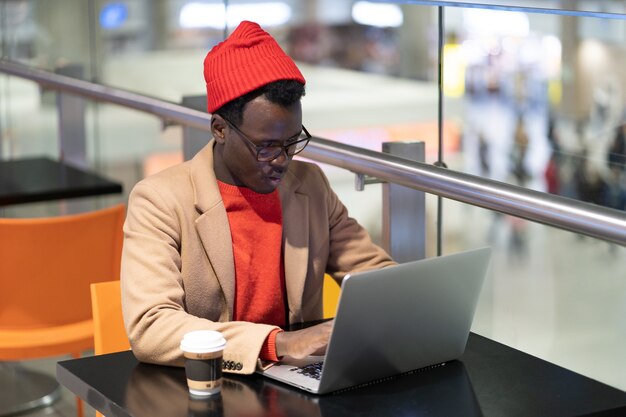 Serious traveler man sitting at cafe in airport work on laptop waiting a boarding