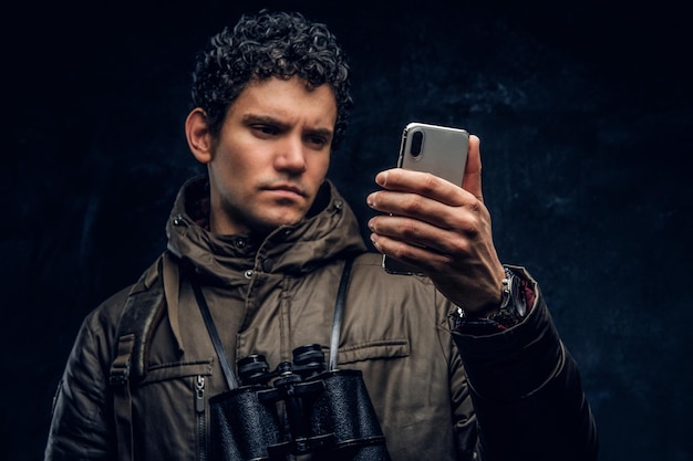 Serious traveler with binoculars looking into the phone on a black background