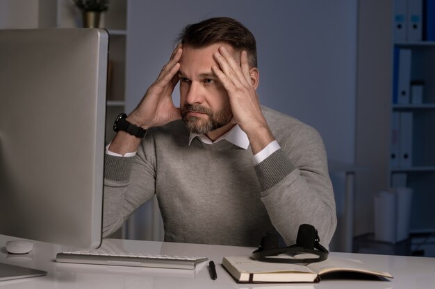 Serious and troubled office worker touching head while working in front of computer screen