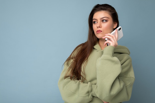 Serious upset attractive young woman wearing stylish hoodie holding using mobile phone