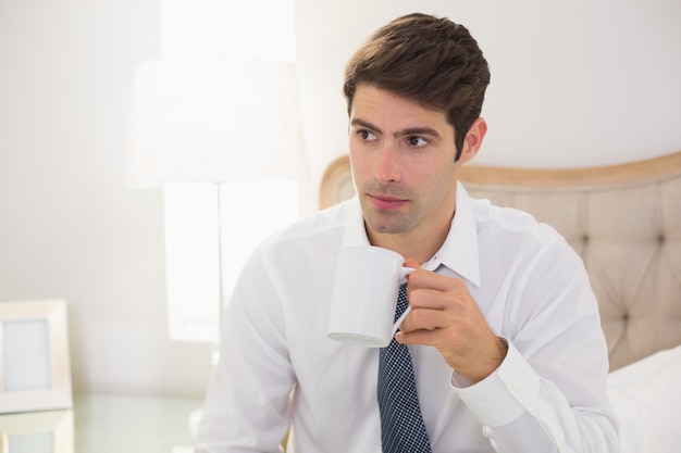 深刻な服を着た男は、ベッドでコーヒーを飲む