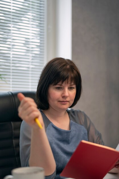 Serious woman chief in her office reads book and drinks coffee. Break time. Lunch time. Secretary writes his plans