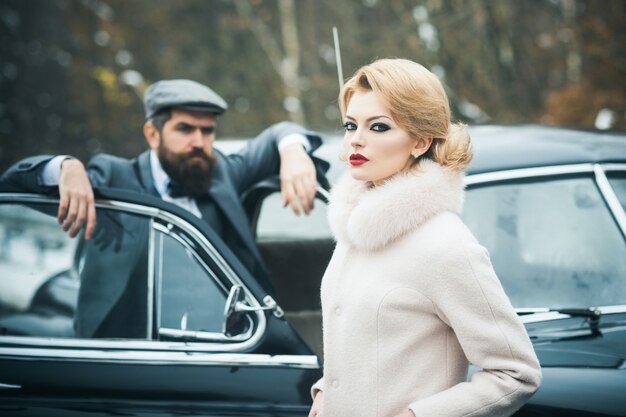 Serious woman in coat and bearded man driver Retro couple near vintage car