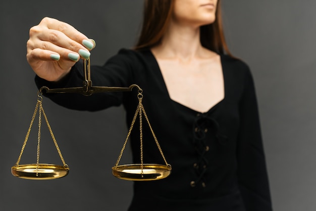 Serious woman holding the justice scale on dark background