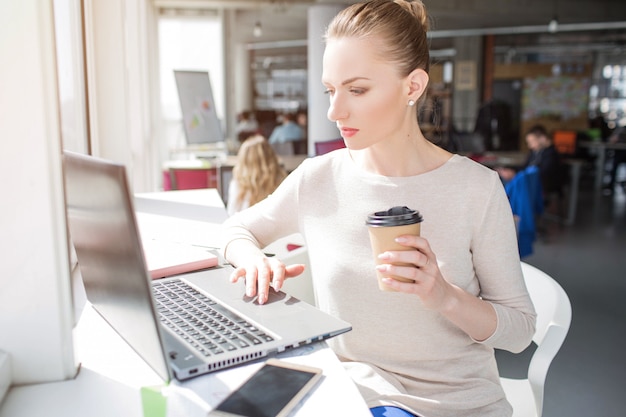 Serious woman is sitting at the table close to the window