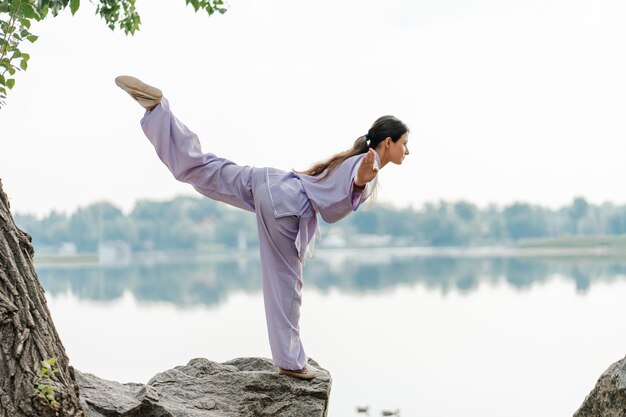 写真 キモノを着た真剣な女性のkungfuマスター ⁇ 水の近くの石の上に立って武術を練習する健康的なライフスタイルの武術コンセプト